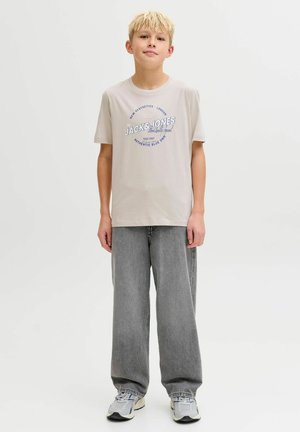 Hele beež värvi t-särk sinise graafilise tekstiga, mida kannab hõbedaste vabaaja laia säärega teksade ja hallide spordijalatsitega. Lihtne disain, vabaaja lõige.