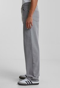 Grey straight-leg jeans made from denim, featuring a classic five-pocket design, stitched detailing, and worn with black and white sneakers.