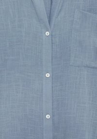 Chemise à manches longues bleu clair en tissu doux et texturé. Présente un motif tissé subtil, une poche poitrine unique et des boutons blancs.