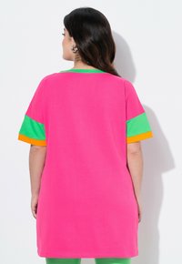 T-shirt surdimensionné rose avec des manches courtes à rayures vertes et orange ; fabriqué en tissu doux, avec un ourlet arrondi.