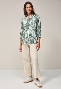 Grön och vit mönstrad skjorta med trekvartslånga ärmar, tillsammans med ljusbeiga vida byxor och vita sneakers.