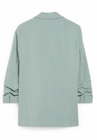 Blazer vert clair à manches longues avec poignets repliés, coutures apparentes et col cranté, vu de dos sur un fond uni.
