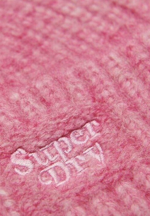 Tissu rose doux et texturé avec le logo blanc brodé "Super Dry" centré dans le cadre.