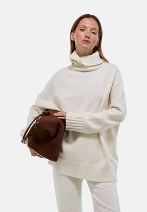 Pull à col roulé oversize couleur crème avec un ourlet et des poignets côtelés, associé à un sac à main en suède marron avec une fermeture à cordon.
