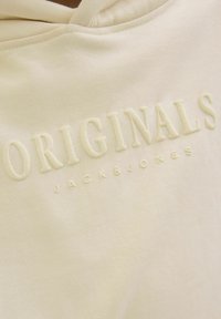 Kremkrāsas kapuces džemperis, izgatavots no mīksta materiāla, ar uzdrukātu "ORIGINALS" tekstu un "JACK & JONES" logotipu diskrētā toņu dizainā.