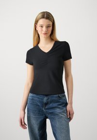 Svart v-hals t-skjorte med korte ermer, med utbrett detaljer i midten og parret med falmede blå jeans. Myk stofftekstur.