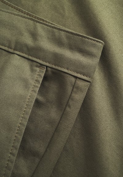 Tissu vert olive avec une surface lisse et texturée. Présente une poche bien visible et des coutures contrastantes. Design durable et structuré.