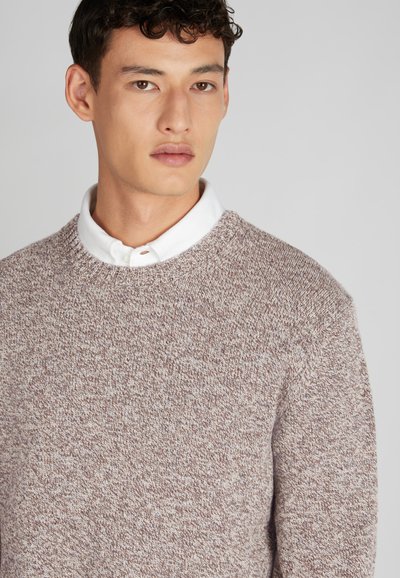 Pull à col rond en maille brune texturée. Présente une chemise col blanc en dessous. Le tissu a un aspect doux et chaud.