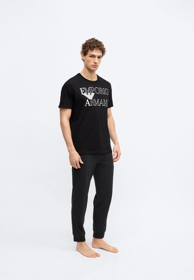 Čierne bavlnené tričko s bielym logom "Emporio Armani", doplnené o čierne nohavice rovnakého štýlu, úzky strih s zúženými manžetami pri členkoch.
