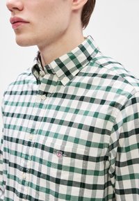 Grønt og hvitt rutet skjorte med knapper som har krage, brystlomme med logo og strukturert stoff.