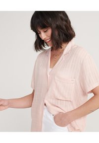 Camicia a maniche corte di colore rosa chiaro, con bottoni e tasca frontale, caratterizzata da un design a righe testurizzato. Tessuto morbido e vestibilità rilassata.