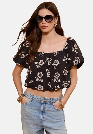 Top corto negro con estampado floral y mangas abullonadas, con escote cuadrado y tela fruncida, combinado con jeans de tiro alto en un tono azul claro.