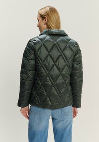 Padded jacket w ciemnozielonym kolorze z diamentowym pikowaniem, z kołnierzem i wyprofilowanymi rękawami. W zestawie z jasnoniebieskimi dżinsami.