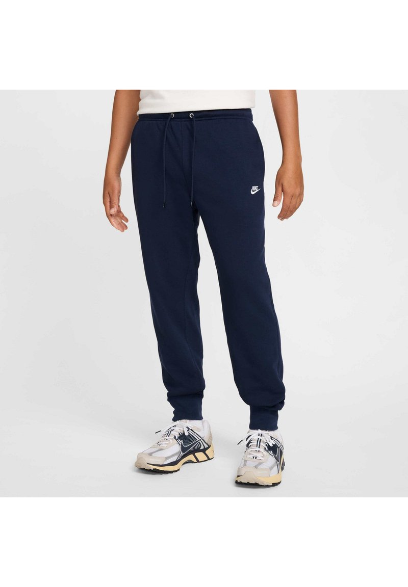 Tengerészeti kék pamut keverék melegítőnadrág, elasztikus derékkal és zsinórral, bordázott mandzsettákkal, valamint egy kis fehér Nike logóval.