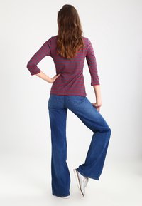 Camicia a maniche lunghe a strisce rosse e grigie abbinata a jeans a zampa d'elefante blu. La camicia presenta maniche tre quarti e un design aderente.