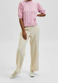 Hellrosa gestrickter Pullover mit Zopfmuster, kurzen Puffärmeln, kombiniert mit weitem, cremefarbenem Hosenbein und weißen Sneakern.