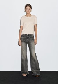 Lys beige t-shirt med korte ærmer, parret med højtaljede, vide, falmede sorte jeans med flossede kanter. Enkel halskæde som accent.