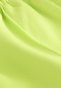 Tissu jaune-vert vif en gros plan montrant une texture lisse et des coutures visibles sous un éclairage doux.