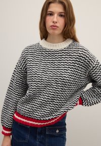 Suéter con patrón en zigzag blanco y negro, cuello de canalé color crema y rayas rojas en el dobladillo y las mangas. Tejido de punto texturizado.