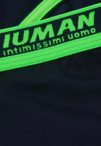 Svart tyg med en texturerad yta, utrustad med ett iögonfallande grönt resårmidjeband med "IUMAN intimiissimi uomo" tryckt i svarta bokstäver.