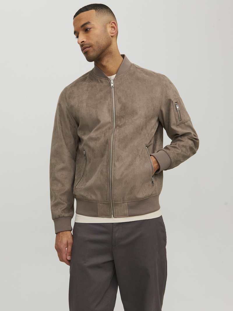 Giubbotto bomber in suede color taupe con zip frontale, polsini e fondo a coste, e tasca laterale con zip, che mostra una texture liscia opaca.