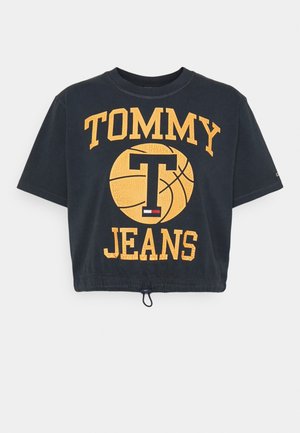 Musta lyhyt crop-top t-paita, jossa on keltainen "TOMMY JEANS" -teksti ja koripallografiikka. Paitassa on kiristysnyöri helman kohdalla ja lyhyet hihat.