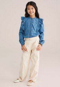 Denimblouse met gerimpelde schouders, knopen aan de voorkant, gecombineerd met crèmekleurige wijde broek en paillettenballetschoenen.