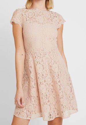 Frau trägt ein kurzärmeliges, hellrosa Spitzenkleid mit Blumenmuster und ausgestelltem Rock.