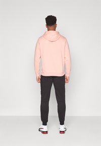 Lichtroze hoodie met een voorzak, een capuchon met trekkoord en geribbelde manchetten, gecombineerd met zwarte taps toelopende joggers en witte sneakers.