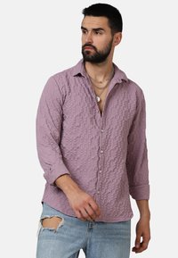 Camicia lavanda textured con chiusura a bottoni e maniche rolled di 3/4, completata da bottoni argentati e una vestibilità comoda. Indossata con denim strappato.