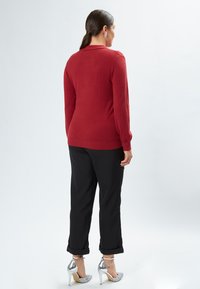 Maglione rosso a maglia con maniche lunghe, abbinato a pantaloni neri arrotolati. Le calzature presentano tacchi alti argentati con cinghie alla caviglia.