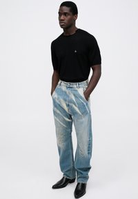 Cămașă tricotată neagră cu mâneci scurte, blugi decolorati albastru deschis cu dungi albe și botas negre cu vârful ascuțit. Design minimalist cu detalii subtile.