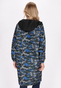 Giacca con motivo mimetico nei toni di grigio, blu e verde, con cappuccio nero e polsini elasticizzati. Vestibilità lunga e rilassata.