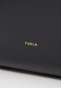 Czarna skórzana torba o gładkiej fakturze, z wyraźnie umieszczonym złotym wytłoczonym logo "FURLA". Minimalistyczny design i smukły kształt.