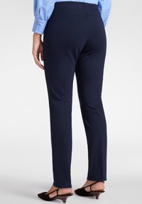 Granatowe dopasowane spodnie o gładkiej teksturze, slim fit i średnim stanie, w połączeniu z brązowymi sandałami na obcasie.