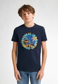 Marineblå bomulds t-shirt med et cirkulært grafisk motiv af bølger og palmetræer i orange og teal, med tekst der omkranser designet.