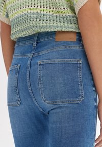 Jeans de mezclilla de un azul claro con una cintura alta, que cuentan con dos bolsillos traseros y un parche de cuero marrón en la cinturilla. Textura suave, ajuste entallado.