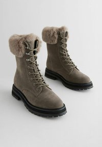 Grå mocka ankstövlar med en faux fur-krage, metalliska öglor och en texturerad svart gummisul. Snörningsdesign med robust konstruktion.