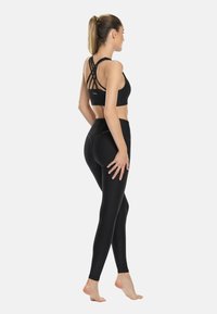 Reggiseno sportivo nero con spalline incrociate sul retro abbinato a leggings neri a vita alta. Tessuto morbido ed elasticizzato con dettagli del logo discreti.
