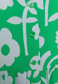 Abito verde con motivo floreale bianco e tessuto testurizzato. Presenta bottoni verdi lungo la parte anteriore, con un dettaglio arricciato all'orlo.
