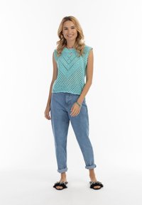 Top senza maniche lavorato a maglia azzurro chiaro con motivo a rombi, abbinato a jeans in denim con risvolto e sandali neri in peluche.
