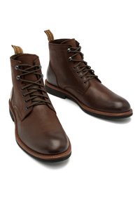 Brązowe skórzane botki za kostkę o gładkim wykończeniu, okrągłych noskach i wiązanym zapięciu. Posiadają teksturowaną podeszwę i pętelkę z tyłu.