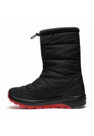 Botte d'hiver noire isolée avec un dessus matelassé, bout rond et semelle texturée noire, avec des accents rouges sur la semelle extérieure et un cordon de serrage en haut.