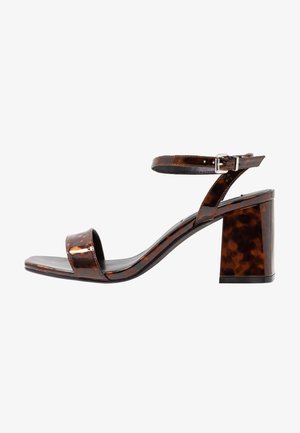 Sandale à talons hauts en écaille de tortue marron avec une sangle de cheville ajustable, un design à bout ouvert et un talon bloc, présentant une finition brillante.