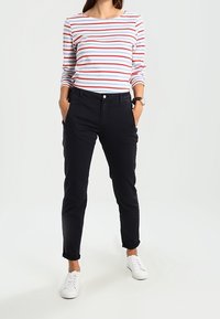 Stripet langærmet top i hvid, blå og rød; sort slim-fit bukser; hvide sneakers med snørebånd synlige; hænderne i lommerne.