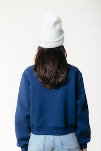 Hanorac cropped albastru marin cu manșete și tiv striate, purtat peste pantaloni scurți din denim bleu deschis cu talie înaltă. Căciulă tricotată albă pe cap.