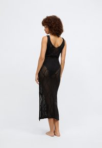 Μαύρο πλεκτό φόρεμα με εφαρμοστή κορσέ και μακριά, ρέουσα φούστα. Διαθέτει ανοιχτό μοτίβο και σχεδίαση V στην πλάτη. Μαλακή, ελαφριά υφή.