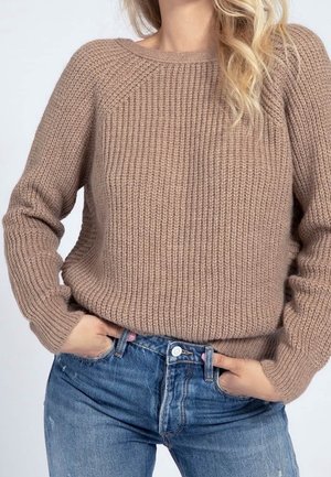 Un pull en maille épaisse couleur brun clair avec une texture côtelée et un décolleté rond, associé à un jean en denim bleu délavé avec un design classique à cinq poches.