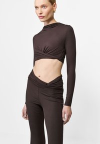 Brązowy, krótkotrwały top z długim rękawem i skręconym przodem, w połączeniu z wysokim, dopasowanym brązowym spodniami o zebranej fakturze.