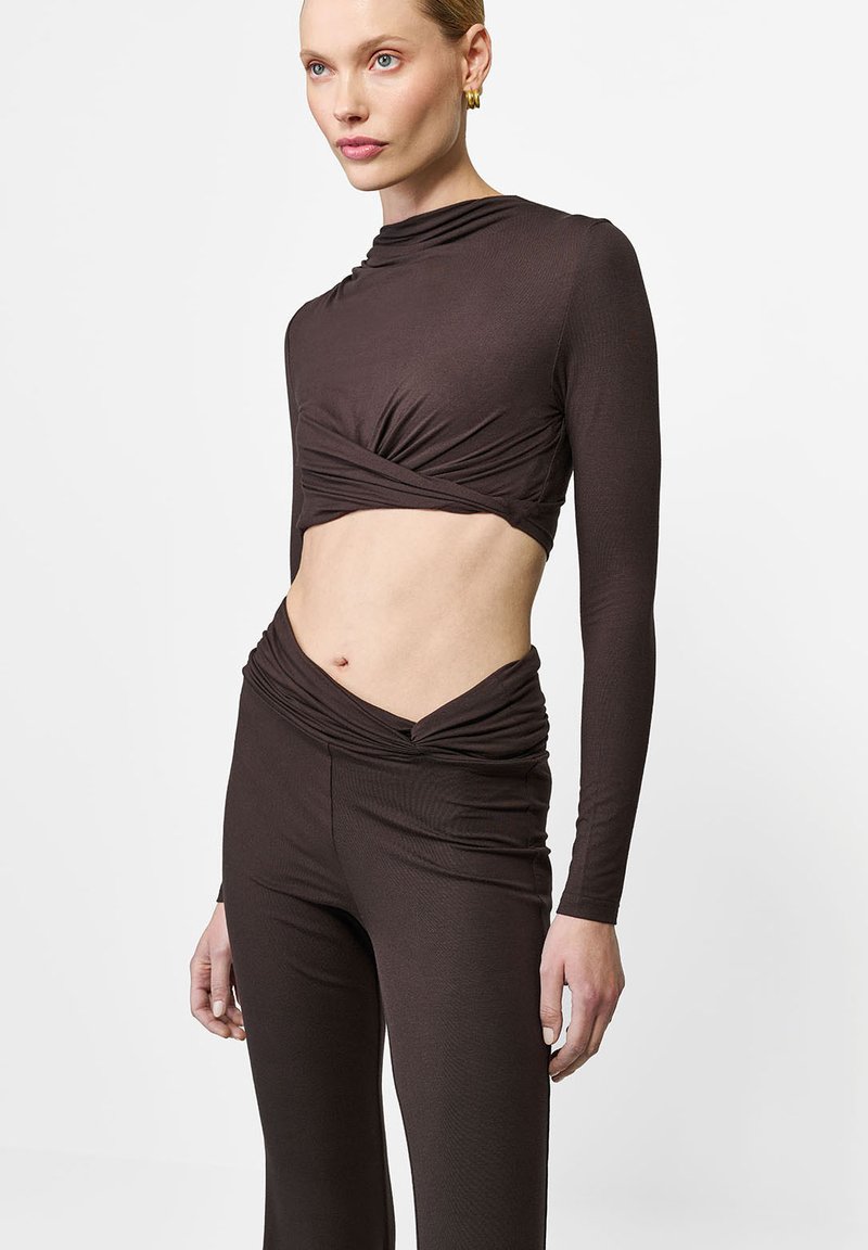 Brązowy, krótkotrwały top z długim rękawem i skręconym przodem, w połączeniu z wysokim, dopasowanym brązowym spodniami o zebranej fakturze.